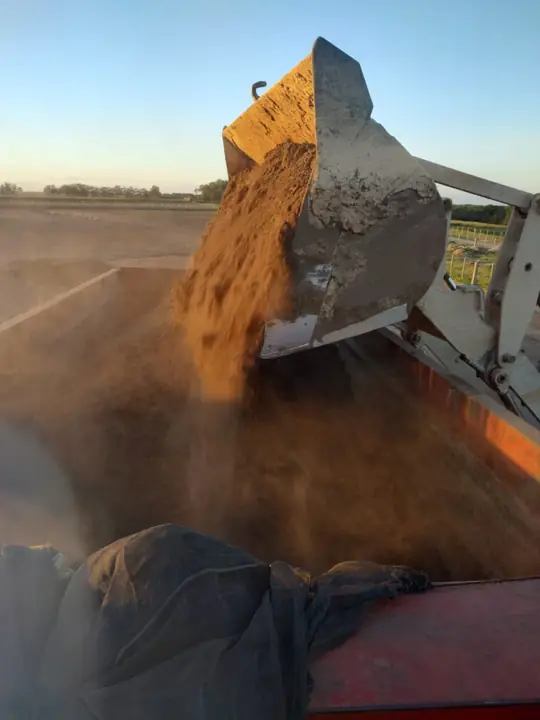 Pá carregadeira despejando material na caçamba de um caminhão
